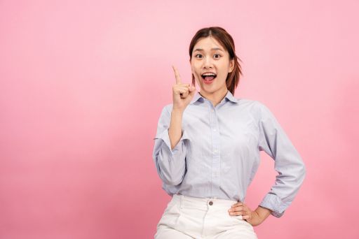 シャツを着た女性が人差し指を立てて笑顔で立っている