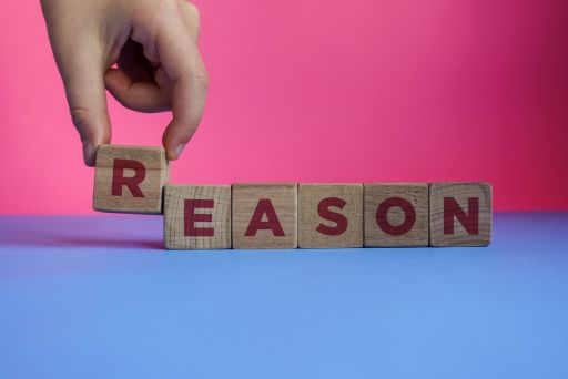 赤い文字でREASONと書かれた木のダイスを持ち上げる様子