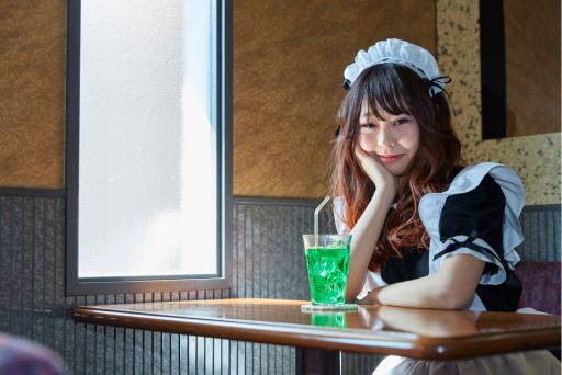 メイド服を着た女性が座っている。メロンソーダが置かれている