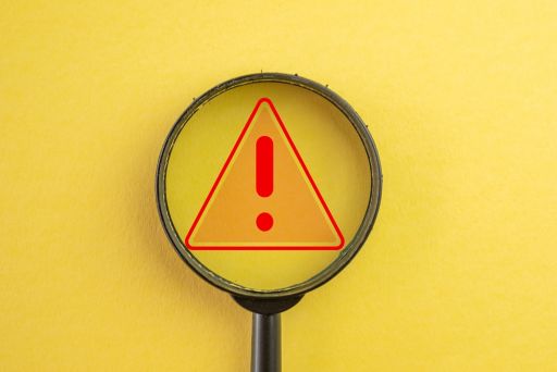 黄色の背景の前にある虫眼鏡と注意マーク