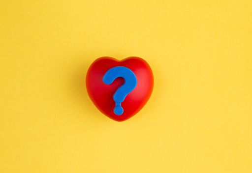 黄色い背景の前にある赤いハートマークに載った青いハテナマーク