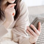 顎に手を当ててスマホを持つ女性