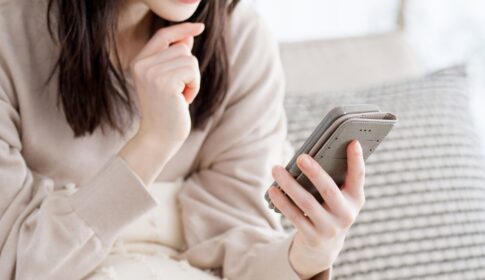 顎に手を当ててスマホを持つ女性