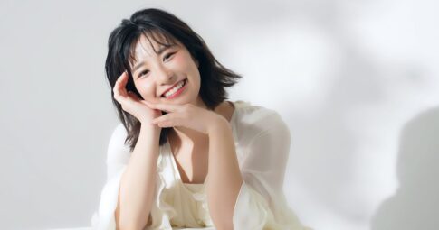 白い服を着て腕に頭を乗せて微笑む若い女性