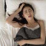 ベッドに横になって頭を抱える女性