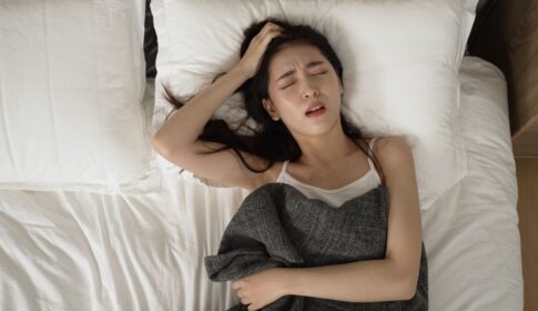 ベッドに横になって頭を抱える女性