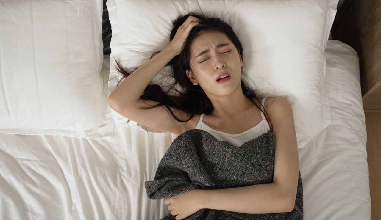 ベッドに横になって頭を抱える女性
