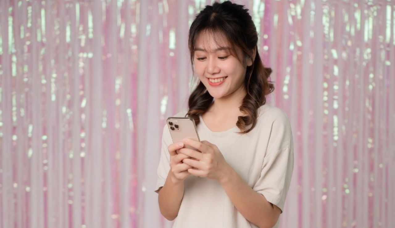 ピンクのキラキラした背景の前でスマホを持って笑顔の女性