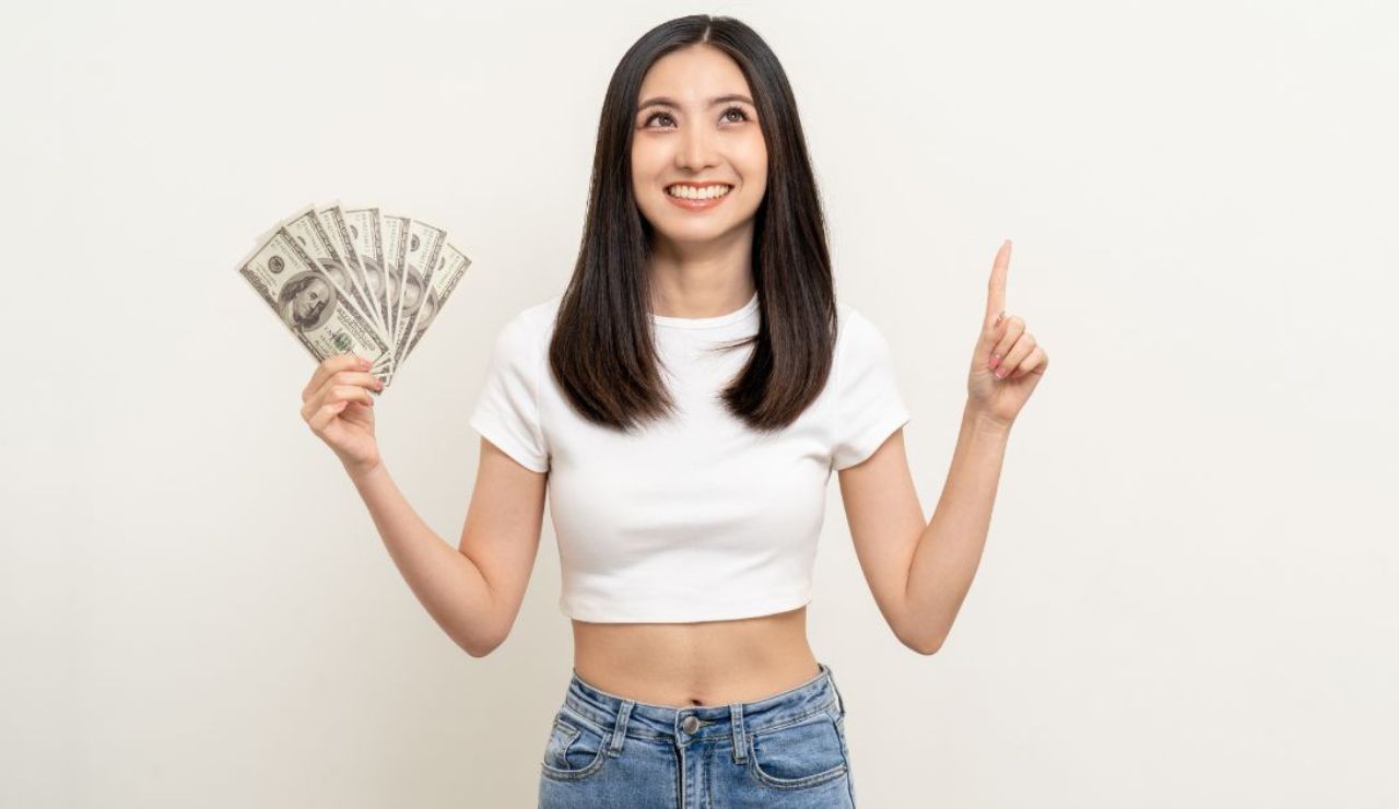 右手で紙幣を持って左手の人差し指を立てる笑顔の黒髪の女性