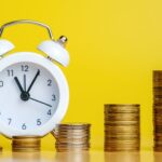 黄色の背景の前にある白い時計と積み上げられたコイン