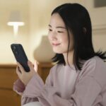 夜の部屋でスマホを見て微笑む女性