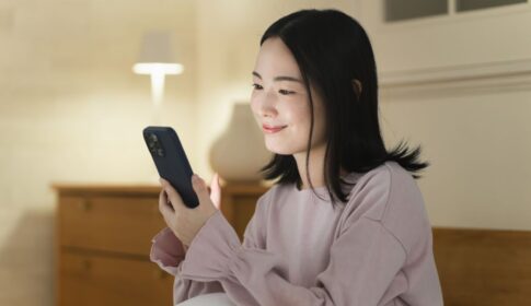 夜の部屋でスマホを見て微笑む女性