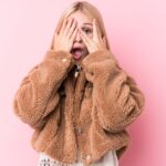 手で顔を隠し片目をあける女性