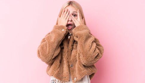 手で顔を隠し片目をあける女性